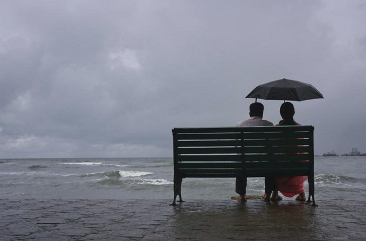 A couple rests on a seaside promenade during a rain shower in Kochi
